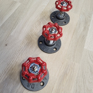 Puede incluir: Tres ganchos de pared de válvula de tubería industrial roja con bridas negras. Cada gancho tiene una válvula redonda roja con la palabra "OPEN" y una flecha impresa en ella. Las bridas están marcadas con "1/2" y "DS".