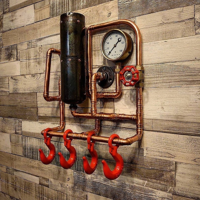 May include: A copper pipe wall mounted coat rack with four red hooks and a round gauge with a white face. The gauge has black numbers and a black needle. The gauge reads 0 to 150.