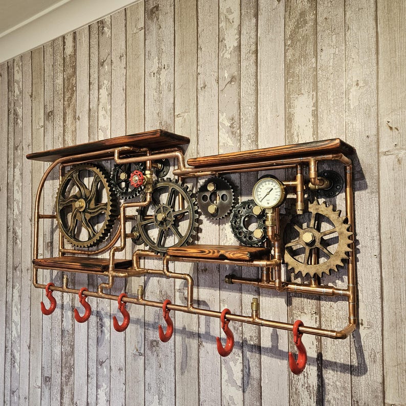 May include: Steampunk-style wall shelf with copper piping, wooden shelves, and decorative gears. Features a pressure gauge and six red hooks for hanging items. The design incorporates industrial and vintage elements.