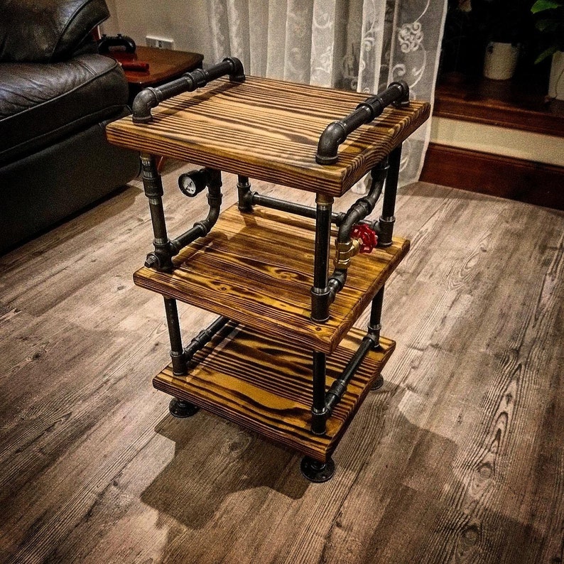 May include: A three-tiered industrial style shelf made from reclaimed wood and black metal pipe fittings. The shelf has a rustic look and is perfect for displaying decorative items or storing small items.