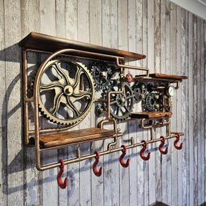 May include: Steampunk-style wall shelf with copper piping, wooden shelves, and decorative gears. Features six red hooks for hanging items. The shelf has a dark wood finish and is mounted on a wooden plank wall.