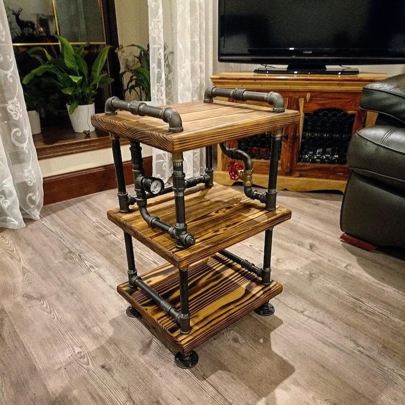May include: A three-tiered side table made of reclaimed wood and black industrial pipe. The table has a rustic look and features a pressure gauge on the middle shelf.
