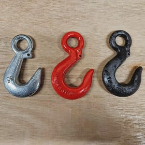 May include: Three metal hooks in silver, red, and black. The silver hook has "UK CA" stamped on it. The red hook has text on it. All hooks have a curved design with a circular opening at the top.