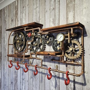 May include: A steampunk-style wall shelf with copper piping, wooden shelves, and decorative gears. Features six red hooks below the lower shelf. The design includes a pressure gauge and a red valve, creating an industrial aesthetic.