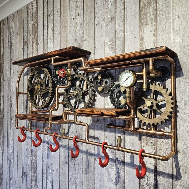 May include: A steampunk-style wall shelf with copper piping, wooden shelves, and decorative gears. Features six red hooks below the lower shelf. The design includes a pressure gauge and a red valve, creating an industrial aesthetic.