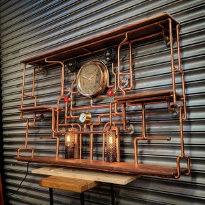 Peut inclure: Étagère murale de style steampunk avec tuyauterie en cuivre, étagères en bois et une horloge vintage. L'unité comprend deux petites lampes avec des abat-jours en treillis métallique et plusieurs jauges et vannes. Le design est industriel et décoratif.