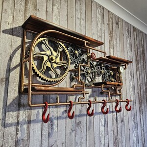 May include: A steampunk-style wall shelf with a copper pipe frame, wooden shelves, and decorative gears. The shelf features six red hooks for hanging items. The gears are in shades of gold, silver, and bronze, creating a unique industrial aesthetic.