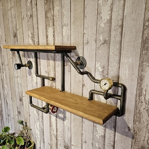 May include: Two-tier industrial wall shelf made from wood and black metal piping. Includes a pressure gauge and a small light. The shelves are made of light-coloured wood.