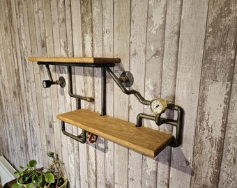 May include: Industrial-style wall shelf with two wooden shelves and black metal piping. Features a pressure gauge and a small light fixture. The shelves are made of light-colored wood.