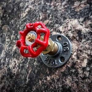 May include: A red industrial pipe valve with a black flange and a 1/2 inch pipe fitting. The valve has a red handle with the words "Open" and "Close" printed on it.