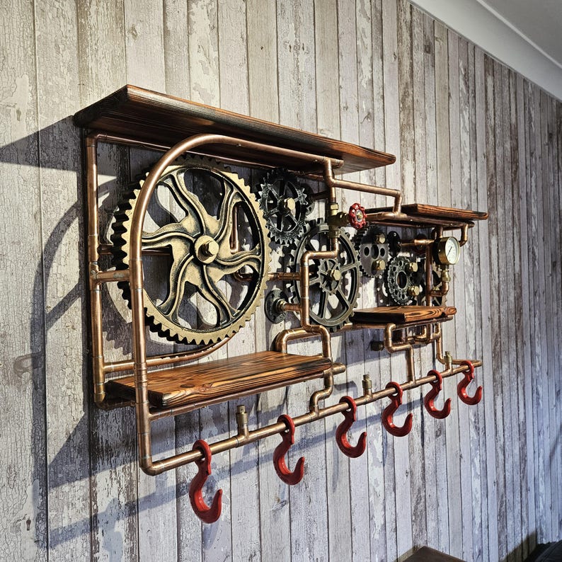 May include: Steampunk-style wall shelf with copper piping, wooden shelves, and decorative gears. Features six red hooks for hanging items. The shelf is mounted on a wooden plank wall.