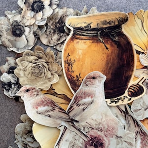 May include: A collection of paper die-cut ephemera featuring two small birds with brown and white feathers, a large amber-colored honey jar with a tied cloth lid, a wooden honey dipper, and various vintage-style floral illustrations in shades of cream, beige, and brown.