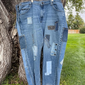 May include: Blue denim jeans featuring a variety of rectangular and square patches in different shades of blue denim fabric. The jeans have a classic five-pocket design, a button fly, and raw, unfinished hems at the bottom of the pant legs.