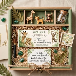 May include: A wooden gift box with a zoo theme, containing a giraffe, lion, and monkey figurines, a pen with a monkey topper, a zoo ticket, and decorative stones. The box includes the text "ZOOBESUCH-GUTSCHEIN" and "Für dich, meine liebe Sophia!"