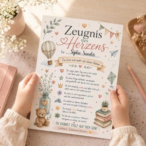 Könnte beinhalten: Eine gedruckte Urkunde mit dem Titel Zeugnis des Herzens für Sophie Sander, verziert mit Aquarellillustrationen eines Heißluftballons, Blumen in einem Glas, eines Teddybären, Büchern und eines Drachens, mit deutschem Text zur Ermutigung.