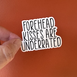 May include: White sticker with black text that reads "Forehead Kisses Are Underrated".