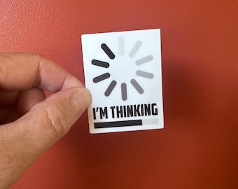 以下が含まれることがあります： 黒とグレーのローディングシンボルと「I'M THINKING」の文字が入った白いステッカー。ステッカーは赤茶色の背景に表示されています。
