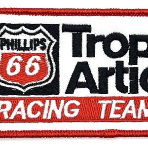 May include: Embroidered patch with a white background and a red border. The patch features the text "Phillips 66" inside a shield, "Trop Artic" in black, and "Racing Team" in white on a red banner. A vintage-style design.