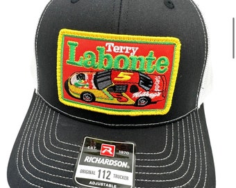 May include: Black and white trucker hat with a red, yellow, and green patch featuring a race car with the text "Terry Labonte" and the number "5". The patch also includes the text "Kellogg's" and "Spongebob". The hat has a white mesh back and a black front with a white stitched border. The hat has a black label with the text "Richardson" and "112 Trucker".