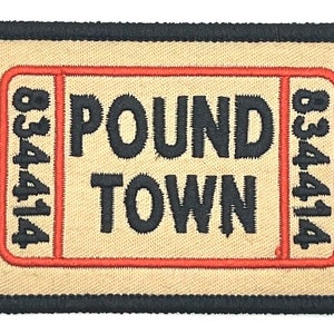 Puede incluir: Un parche bordado beige con un borde negro. El parche presenta un diseño rojo en forma de boleto con el texto "POUND TOWN" y el número "834414" a cada lado.