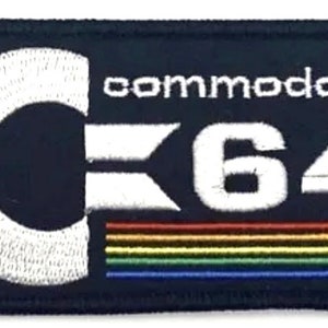 Op de afbeelding: Een blauwe geborduurde patch met een wit C64-logo en het woord "commodore" erboven. Het logo heeft een witte C met een diagonale lijn erdoorheen en het getal 64. De patch heeft een regenboogstreep aan de onderkant.