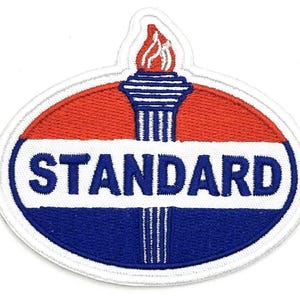 May include: A white oval patch with a red, white, and blue design. The center of the patch features a white torch with a red flame and the word "STANDARD" in blue lettering.