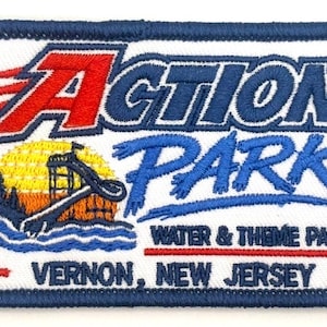 May include: A rectangular embroidered patch with a dark blue border. It features the text Action Park in red and blue, a yellow sun, a water slide, and trees. Below, it reads Water & Theme Park and Vernon, New Jersey in blue text.
