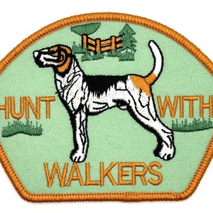 May include: A green and orange embroidered patch with a black and white dog, a fence, and trees. The text "Hunt with Walkers" is embroidered in orange.