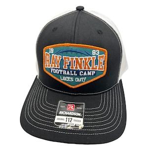 Puede incluir: Gorra de camionero negra y blanca con un parche azul verdoso, naranja y blanco que dice "Ray Finkle Football Camp Laces Out!" con los números 19 y 83 a cada lado del parche. La gorra tiene un logotipo de Richardson y dice "Original 112 Trucker".