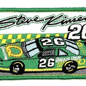 May include: Green and yellow race car with the number 26 on the side and the name Steve Kinser in black cursive writing. The car is on a gray track with a checkered start/finish line.