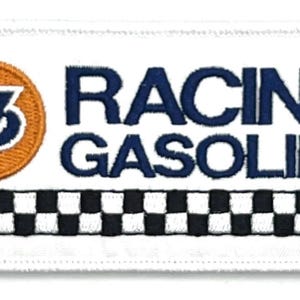 May include: White patch with a blue and orange circle with the number 76 inside. The text "RACING GASOLINE" is in blue letters below the circle. A black and white checkered pattern is at the bottom of the patch.
