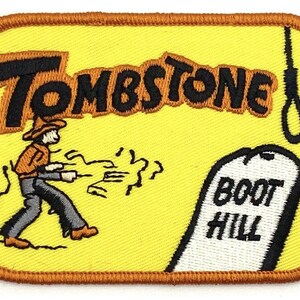 May include: Yellow embroidered patch with a cartoon cowboy running away from a noose and a tombstone that reads "Boot Hill". The text "Tombstone" is above the cowboy.