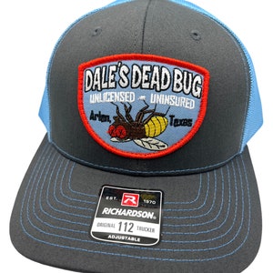 Peut inclure: Casquette de camionneur grise et bleue avec un écusson "DALE'S DEAD BUG" et une illustration d'insecte. La casquette est ajustable et porte une étiquette Richardson.