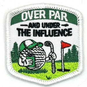 May include: Embroidered patch with the text "OVER PAR - AND UNDER THE INFLUENCE." The patch features a golf ball character wearing a green hat and holding a golf club. A red flag and green trees are also depicted.