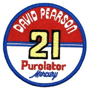 May include: A round, blue-bordered patch with a red background. The text "David Pearson" is written in white around the edge of the patch. The number "21" is in the center of the patch in yellow with a black outline. The text "Purolator Mercury" is written in white below the number.