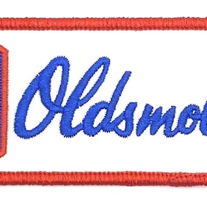 Może przedstawiać: Czerwona naszywka haftowana z białym tłem. Naszywka zawiera niebiesko-białe logo ze stylizowanym grotem strzały i napisem "Oldsmobile" w niebieskim, ozdobnym pismem.