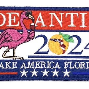 May include: A blue, red, and white embroidered patch with a pink flamingo wearing sunglasses and holding a glass of wine. The patch says "DeSantis 2024" and "Make America Florida" with five white stars below the text.