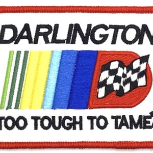 May include: A white embroidered patch with red trim featuring the text "DARLINGTON" in black, a rainbow-colored stripe design, a checkered flag, and the text "TOO TOUGH TO TAME" in black.