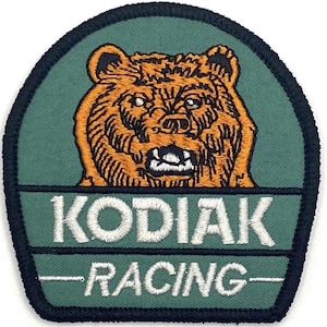 May include: Embroidered patch featuring a detailed orange bear head on a green background. The text "KODIAK RACING" is displayed in white lettering. The patch has a dark green border.