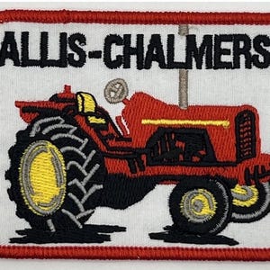 May include: Embroidered patch showing a red tractor with black tyres and yellow details. The patch has the text "ALLIS-CHALMERS" in black letters on a white background, framed by a red border. A vintage-style design.