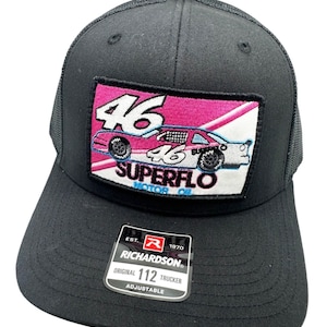 May include: Black trucker hat with a pink and white patch featuring a racing car with the number 46 and the text "SUPERFLO MOTOR OIL". The hat has a black mesh back and an adjustable strap with the Richardson logo and the text "EST. 1970 ORIGINAL 112 TRUCKER ADJUSTABLE".