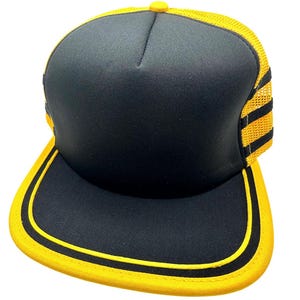 May include: Black and yellow trucker hat with a mesh back and a curved brim. The front panel is black, and the brim and trim are yellow. The hat has a yellow button on top.