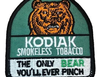 May include: Embroidered patch featuring a detailed orange bear illustration over a green background. The patch reads "KODIAK SMOKELESS TOBACCO" and "THE ONLY BEAR YOU'LL EVER PINCH" in white and green text.