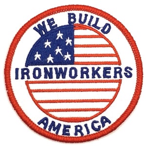 May include: Embroidered patch with a circular design featuring the American flag. The top portion is blue with white stars, and the bottom has red and white stripes. Text includes "WE BUILD IRONWORKERS AMERICA" in blue and white.