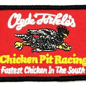 May include: Embroidered patch with a red background, black border, and white text that reads "Clyde Forkel's Chicken Pit Racing Fastest Chicken In The South." A black and white chicken graphic is in the center.