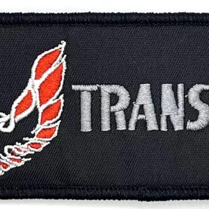 Könnte beinhalten: Schwarzer gestickter Aufnäher mit einem roten und weißen Vogellogo und dem Text "TRANS AM" in Silber.