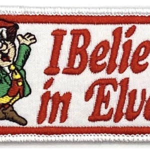 Puede incluir: Parche bordado con borde rojo y el texto "I Believe in Elves". El parche presenta un elfo de dibujos animados con sombrero rojo, chaqueta verde y zapatos marrones. El elfo sonríe y saluda.