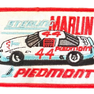 May include: A white and blue racing car with the number 44 on the side. The car is on a white background with the words "Sterling Marlin" and "Piedmont" in red.
