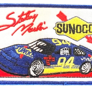 May include: A blue and yellow race car with the number 94 on the side. The car is on a red and white background with the words "Sunoco" and "Sterling Marlin" in red.