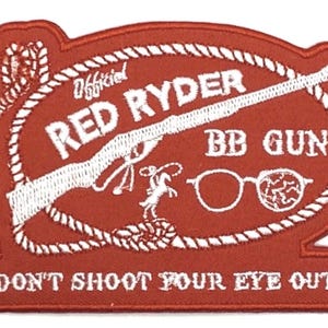 May include: A red and white embroidered patch with the words "Official Red Ryder BB Gun" and the phrase "Don't Shoot Your Eye Out!" The patch features a rifle, cowboy, and glasses.